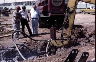 Bustin' rocks: the Vulcan DGH-100 hammer on a backhoe adapter during Vulcan's plant expansion in 1979. Left to right watching the hammer: (in hardhat) Gene Daniels, Vulcan's Construction Manager for the project; Kurt Winters, Onshore Sales Manager, and W. Calvin Bridges, Executive Vice President.